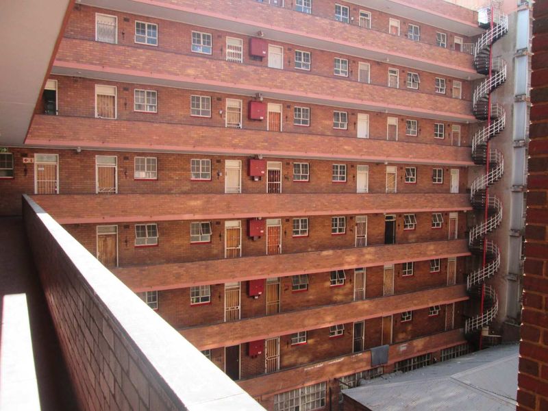 Exterior view of a multi-story apartment building featuring brick facade, open-air balcony walkways, and an external spiral staircase.