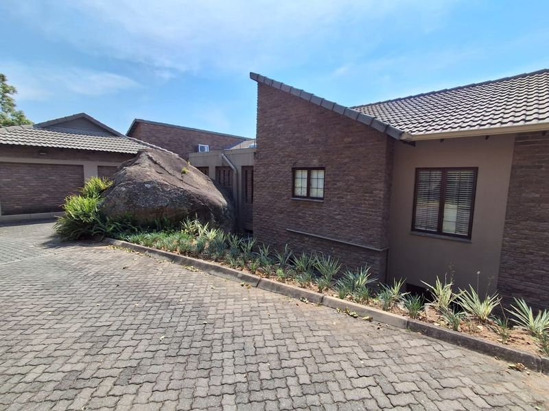 Front exterior view of the apartment complex featuring a brick facade, tiled roof, and a paved driveway with landscaped garden beds.