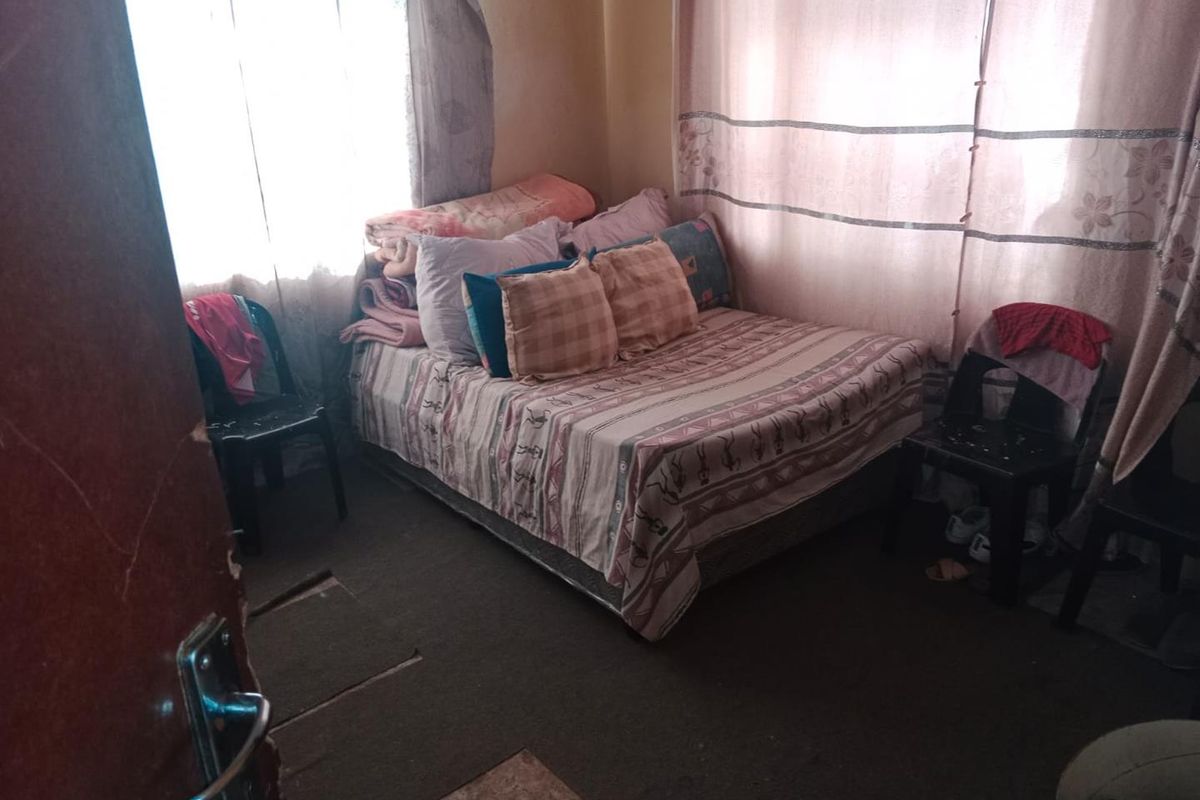 A compact bedroom featuring natural light through windows with curtain rails and worn flooring, requiring cosmetic updates to improve the overall living space.