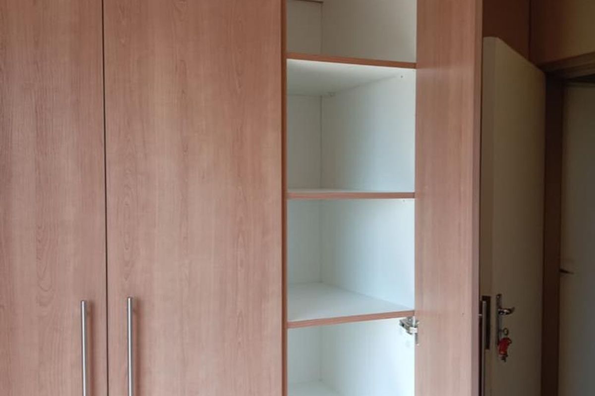 A built-in bedroom wardrobe featuring light wood-grain laminate doors with modern metal handles and internal shelving.
