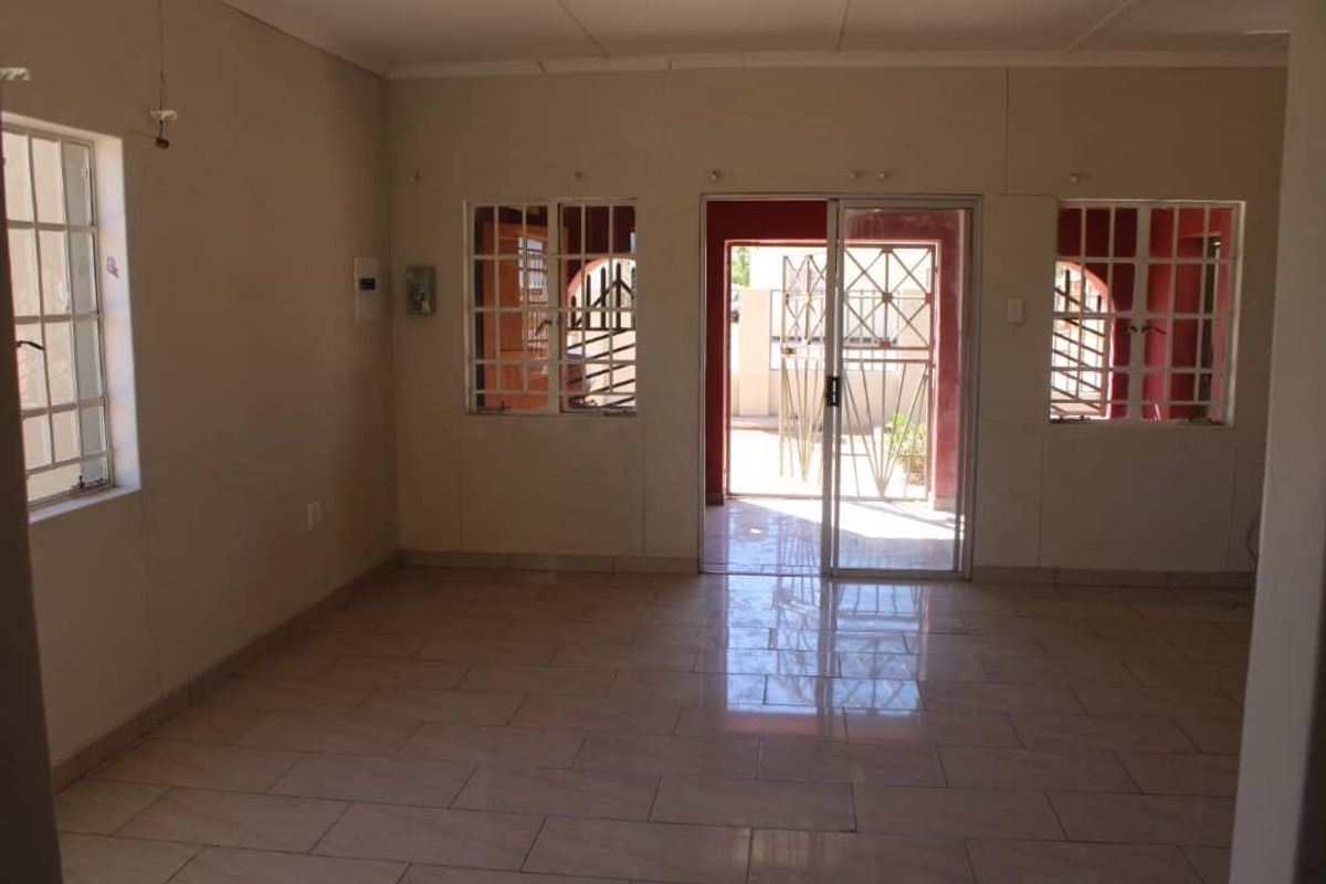 An empty living room featuring tiled flooring, security bars on windows, and a sliding glass door leading to an outdoor area.