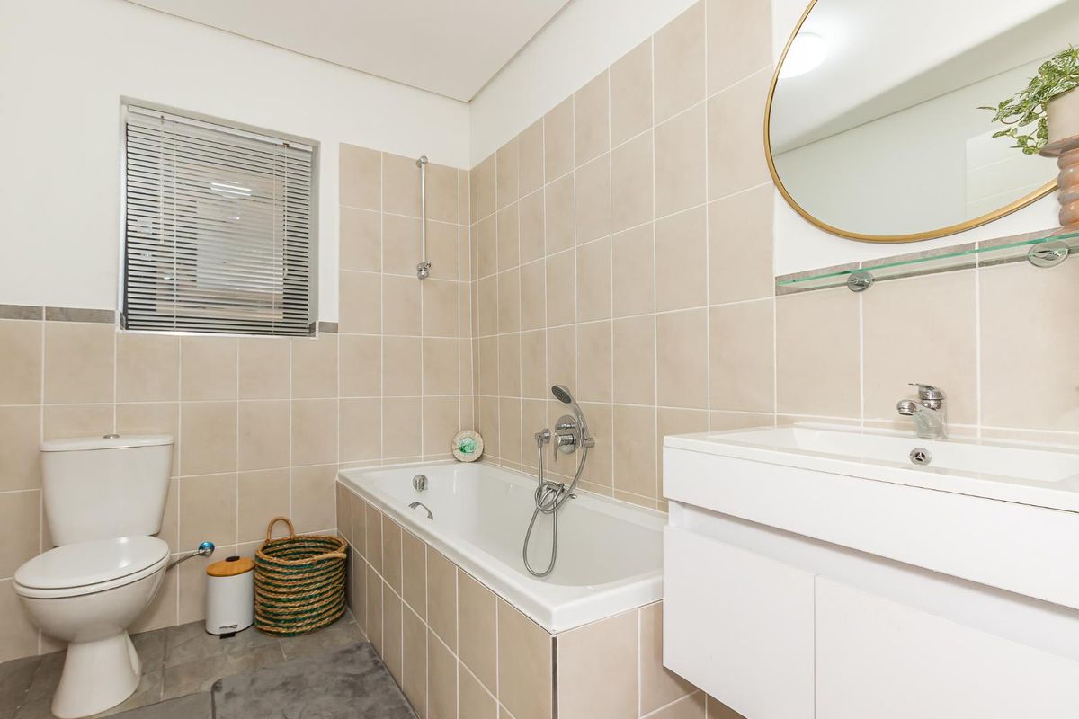 A clean, functional bathroom featuring a built-in bathtub with shower mixer, a wall-mounted vanity with basin, and neutral wall tiling.