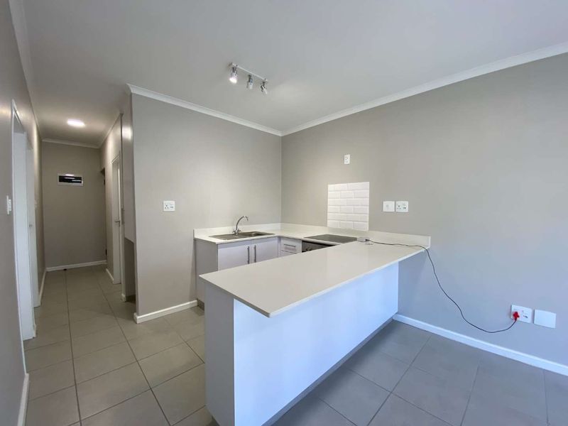 Modern open-plan kitchen featuring stone countertops, a breakfast bar, electric hob, and neutral tiled flooring in a clean, well-maintained space.
