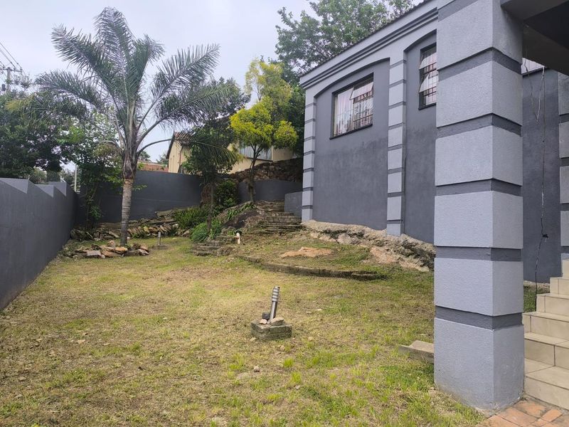 Rear garden area featuring a lawn, stone steps, retaining walls, and exterior lighting, adjacent to the main house structure.