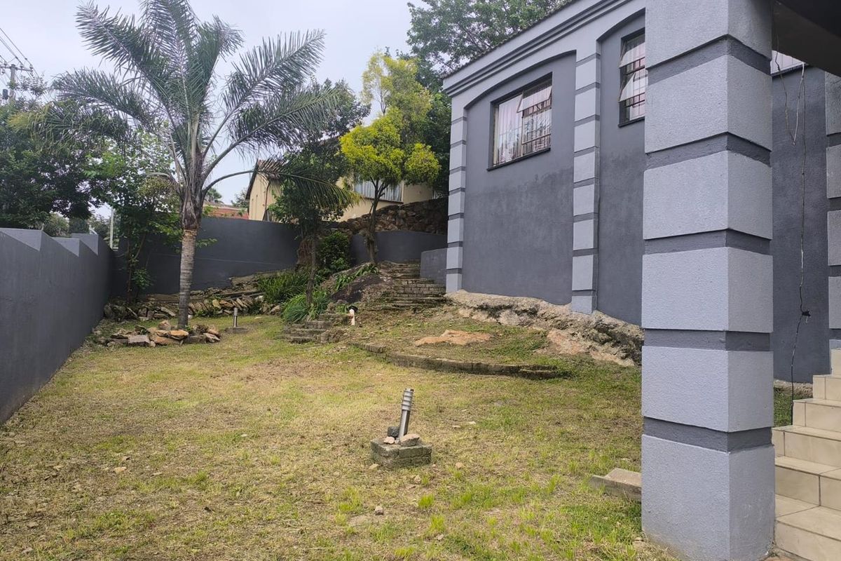 Rear garden area featuring a lawn, stone steps, retaining walls, and exterior lighting, adjacent to the main house structure.