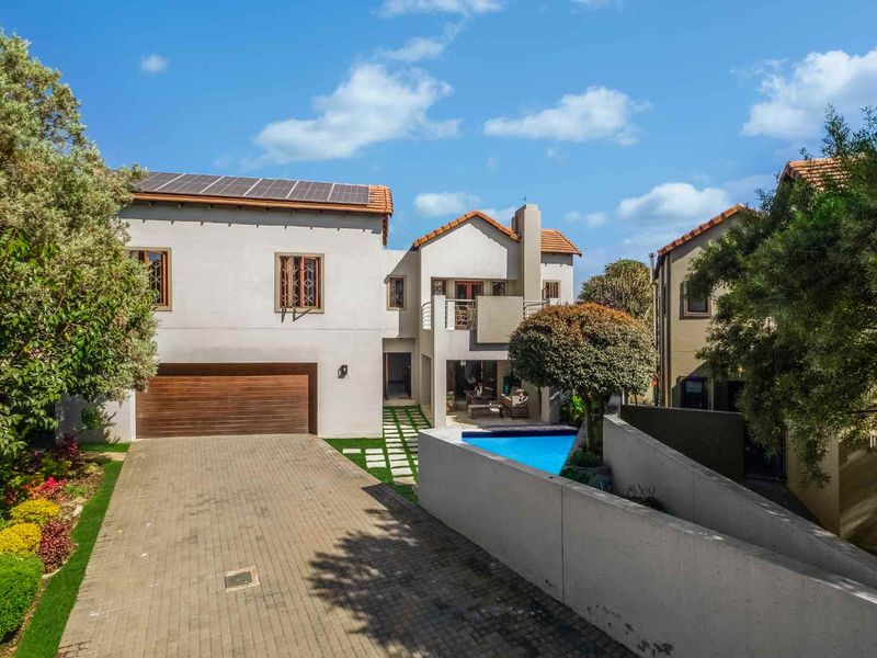 A well-maintained multi-story residential property featuring a paved driveway, integrated garage, swimming pool, and rooftop solar panels.