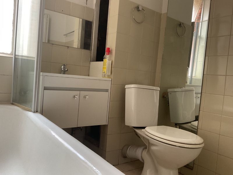 A dated bathroom featuring a bathtub, vanity cabinet, and toilet, currently requiring maintenance and cosmetic updates to the wall finishes and tiling.