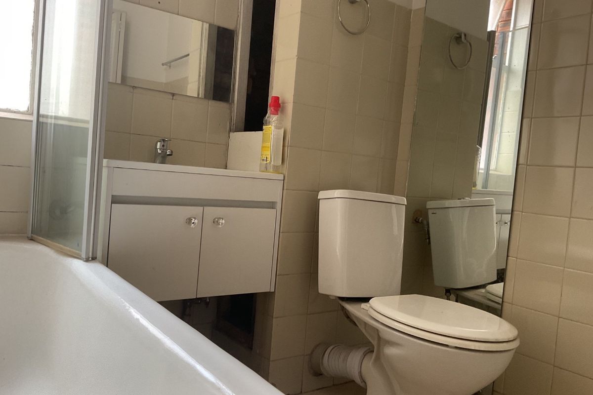 A dated bathroom featuring a bathtub, vanity cabinet, and toilet, currently requiring maintenance and cosmetic updates to the wall finishes and tiling.