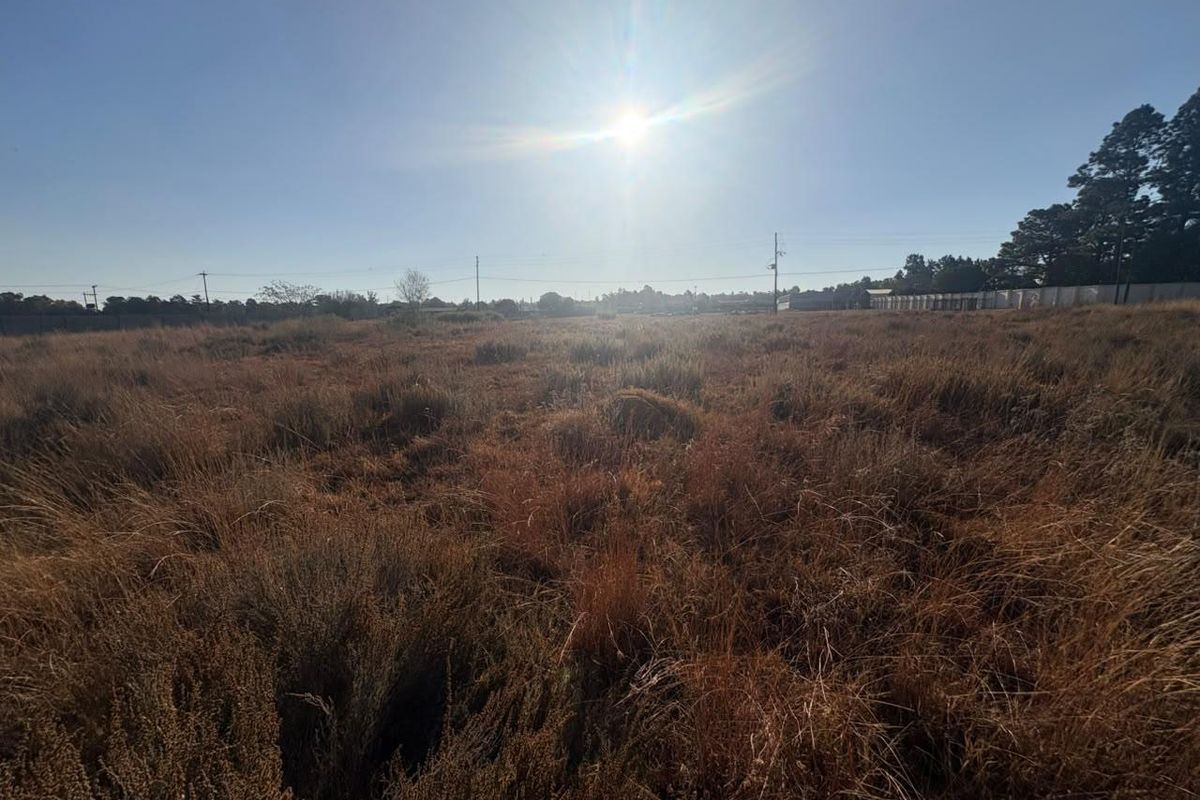 A wide-angle view of a vacant residential plot featuring natural vegetation and open space, suitable for future development.