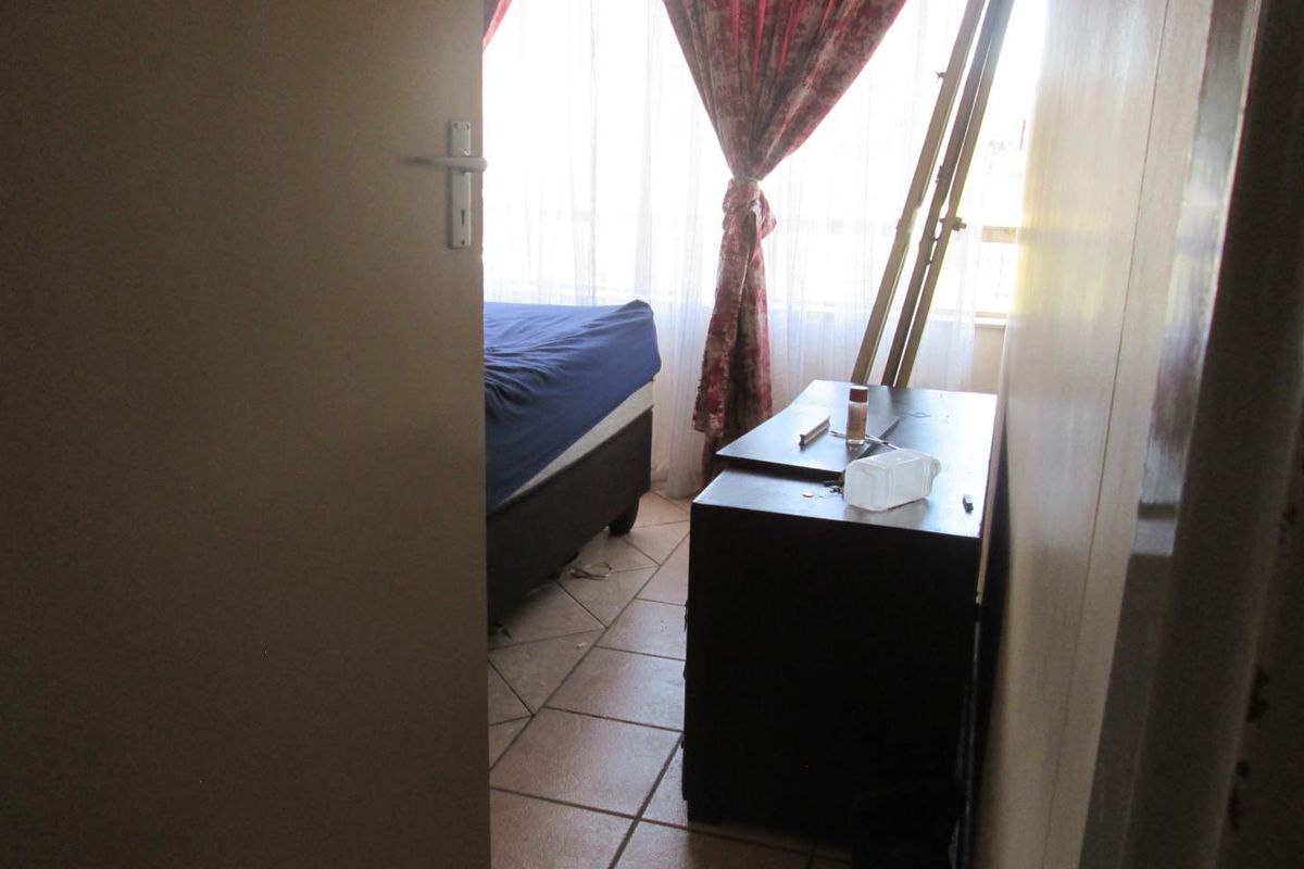 A view into a bedroom featuring tiled flooring, captured from the doorway with natural light filtering through window curtains.