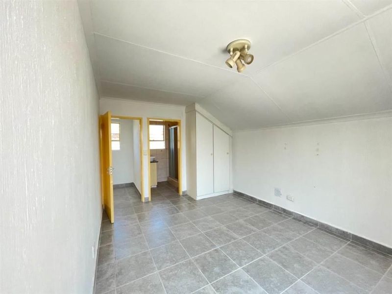 An empty bedroom featuring tiled flooring, a sloped ceiling, and a built-in cupboard, with an adjoining bathroom area.