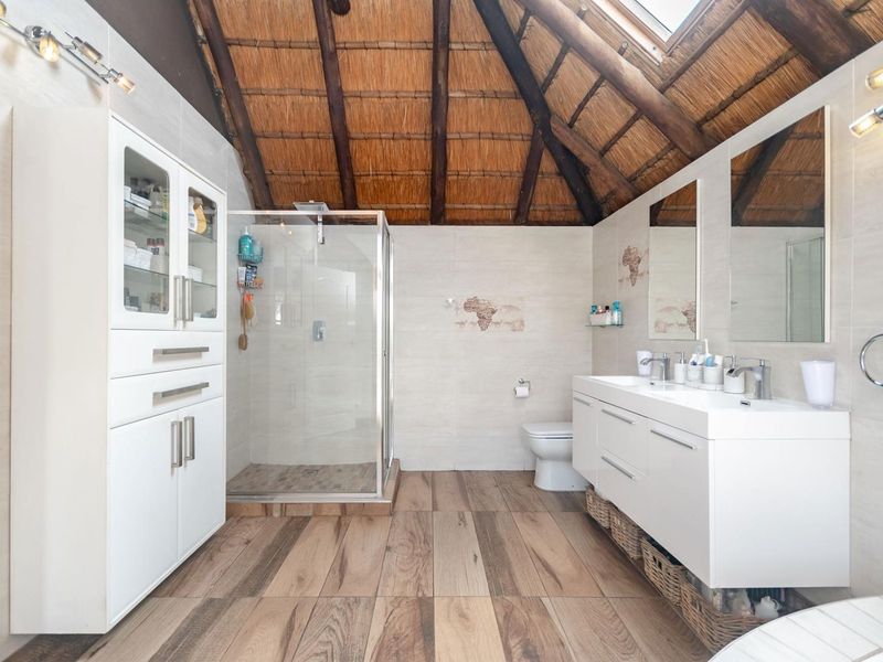 A well-maintained bathroom featuring a double vanity, glass shower enclosure, built-in cabinetry, and a unique thatched roof ceiling with a skylight.