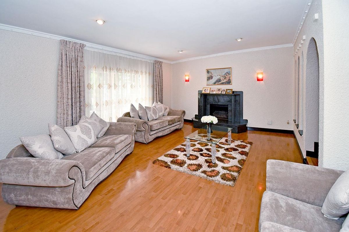 A spacious living room featuring polished wooden flooring, a built-in stone fireplace, and recessed ceiling lighting.