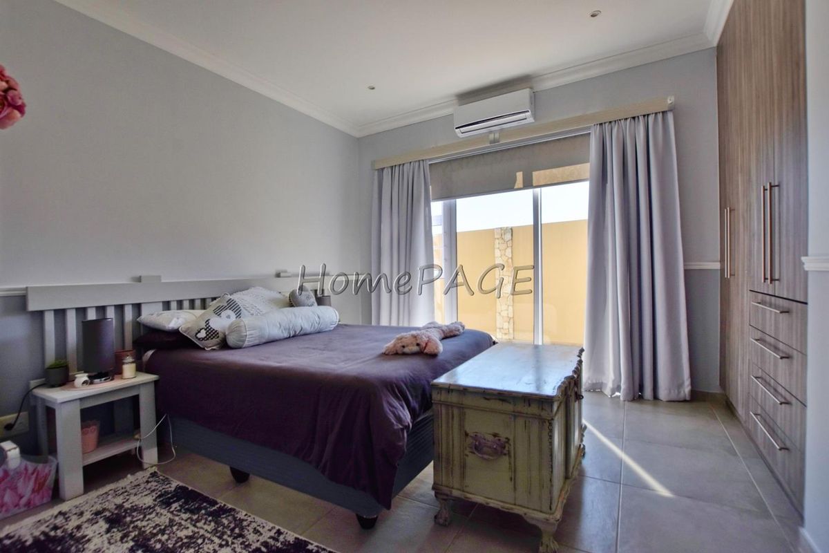 A well-maintained bedroom featuring built-in wooden cabinetry, tiled flooring, and a wall-mounted air conditioning unit with direct access to an outdoor area.