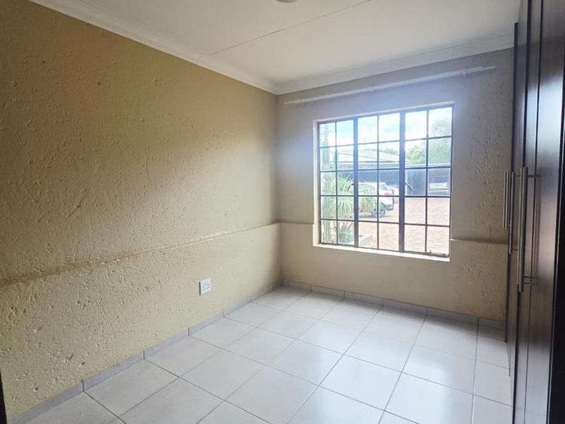 A clean, empty bedroom featuring tiled flooring, built-in cupboards, and a grid-pattern window providing natural light.