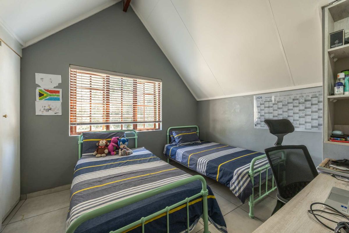 A bedroom featuring a vaulted ceiling, tiled flooring, built-in shelving, and a window with venetian blinds.
