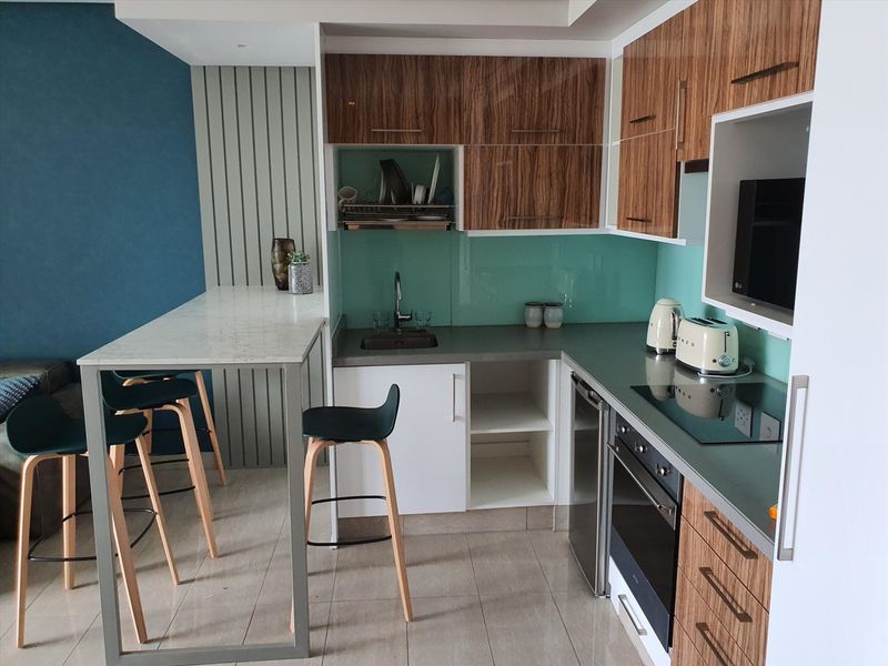 Modern kitchen featuring wood-grain cabinetry, stone countertops, glass splashback, integrated appliances, and a functional breakfast bar area.