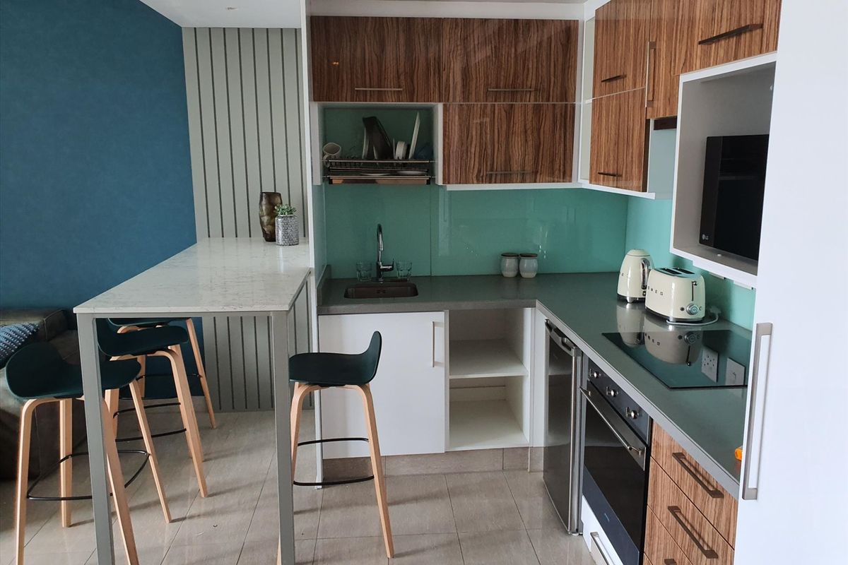 Modern kitchen featuring wood-grain cabinetry, stone countertops, glass splashback, integrated appliances, and a functional breakfast bar area.