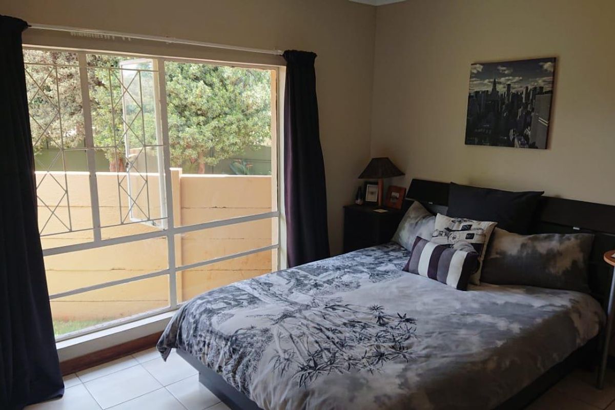 A bedroom featuring tiled flooring and a large window with security bars, providing natural light and views of the exterior wall.