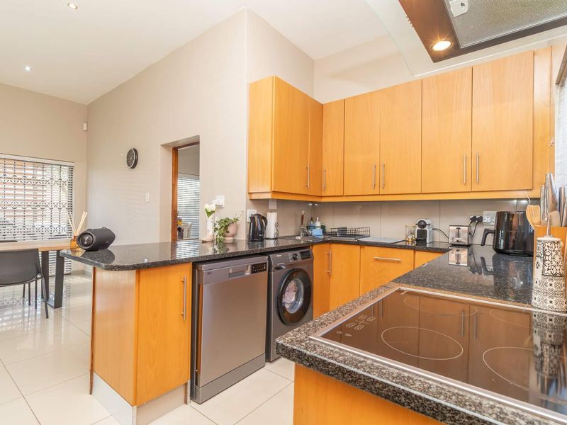 A functional kitchen featuring light wood cabinetry, granite countertops, an integrated electric hob with extractor fan, and tiled flooring in an open-plan layout.