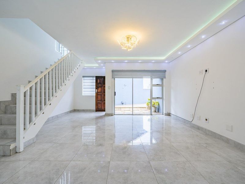 Spacious, bright living area featuring polished tile flooring, a modern staircase, and sliding glass doors leading to an outdoor space.