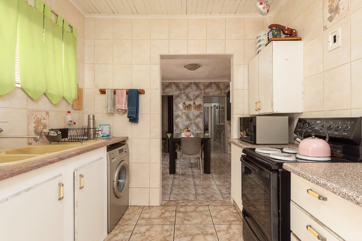 A functional kitchen featuring tiled walls and floors, built-in cabinetry, a double basin sink, and a freestanding stove, with an adjacent dining area.