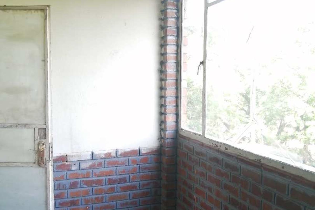 An empty room featuring exposed brick wall accents, large windows, and a simple door, offering a blank canvas for renovation or interior design updates.
