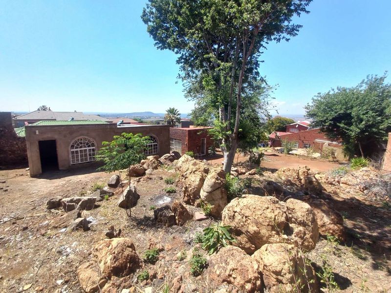 A rear exterior view of the property featuring brick structures, arched windows, and a natural rocky garden area.