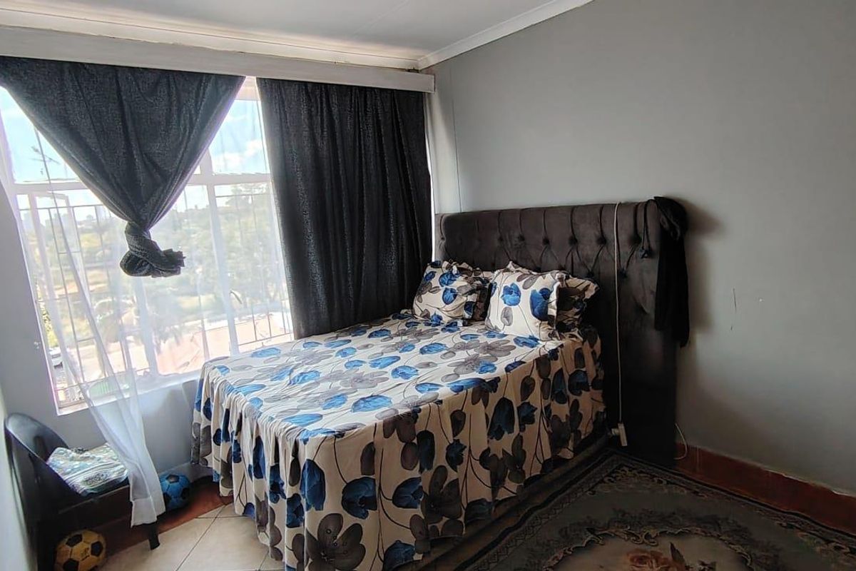 A functional bedroom featuring a large window that provides natural light, tiled flooring, and neutral wall finishes.