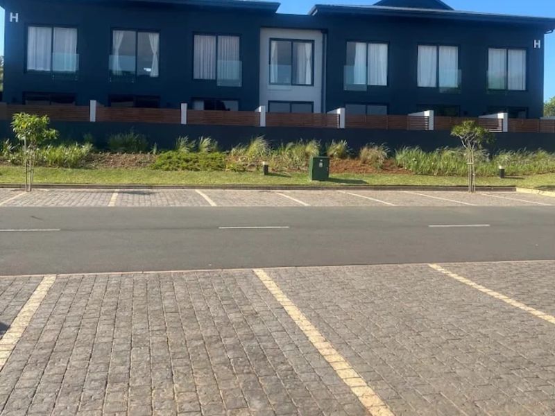 Front elevation of a modern apartment complex featuring dark facade, glass balustrades, and a paved parking area.