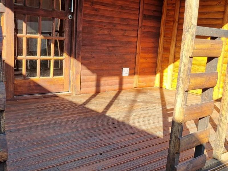 A covered timber deck patio featuring wooden balustrades and direct access to the cottage interior through a glass-paned door.