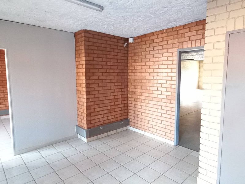 An industrial office space featuring exposed brickwork, tiled flooring, and multiple doorways leading to adjacent work areas.