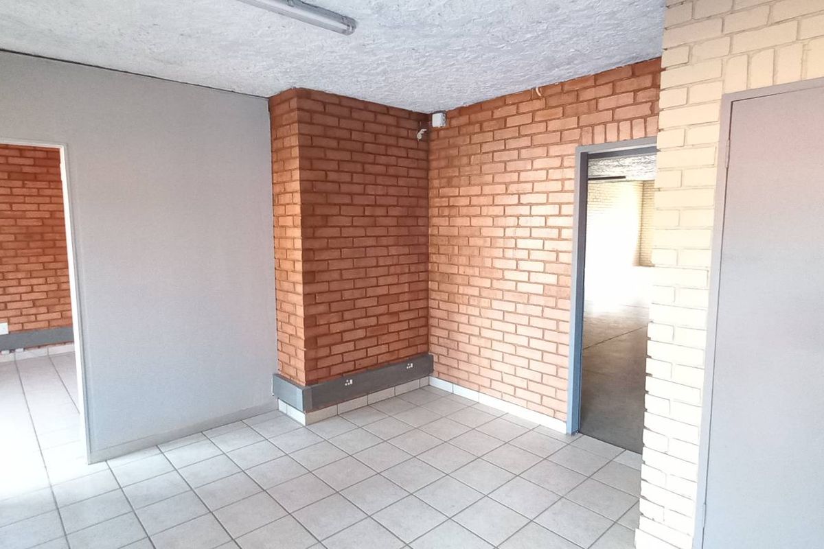 An industrial office space featuring exposed brickwork, tiled flooring, and multiple doorways leading to adjacent work areas.