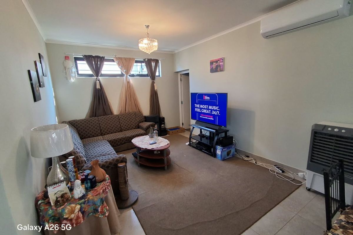 A living room featuring tiled flooring, a wall-mounted air conditioning unit, and horizontal windows, providing a functional and comfortable living space.