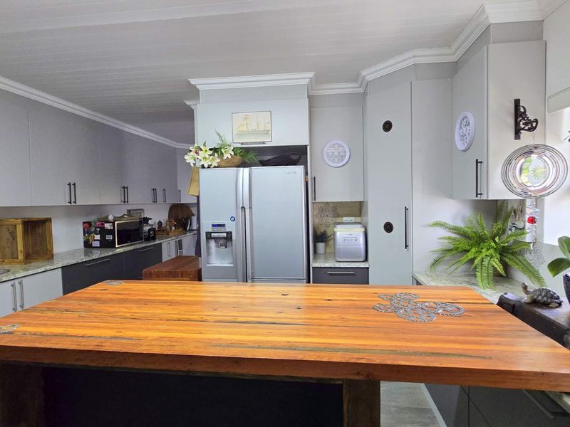 Modern kitchen featuring grey cabinetry, granite countertops, an undermount sink, and a prominent wooden island, complemented by crown molding and a tongue and groove ceiling.
