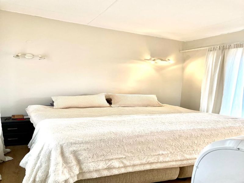 A neutrally decorated bedroom featuring wall-mounted lighting and window curtain tracks, providing a comfortable and functional sleeping space.