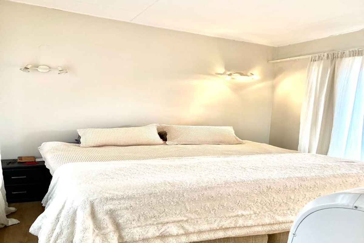 A neutrally decorated bedroom featuring wall-mounted lighting and window curtain tracks, providing a comfortable and functional sleeping space.