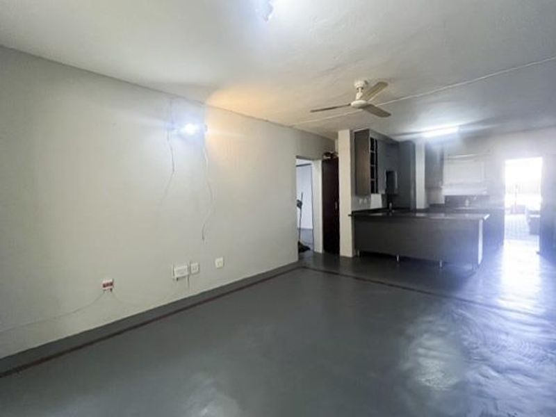 An open-plan living and kitchen area featuring a central island, ceiling fan, and neutral finishes, currently vacant and ready for renovation or staging.