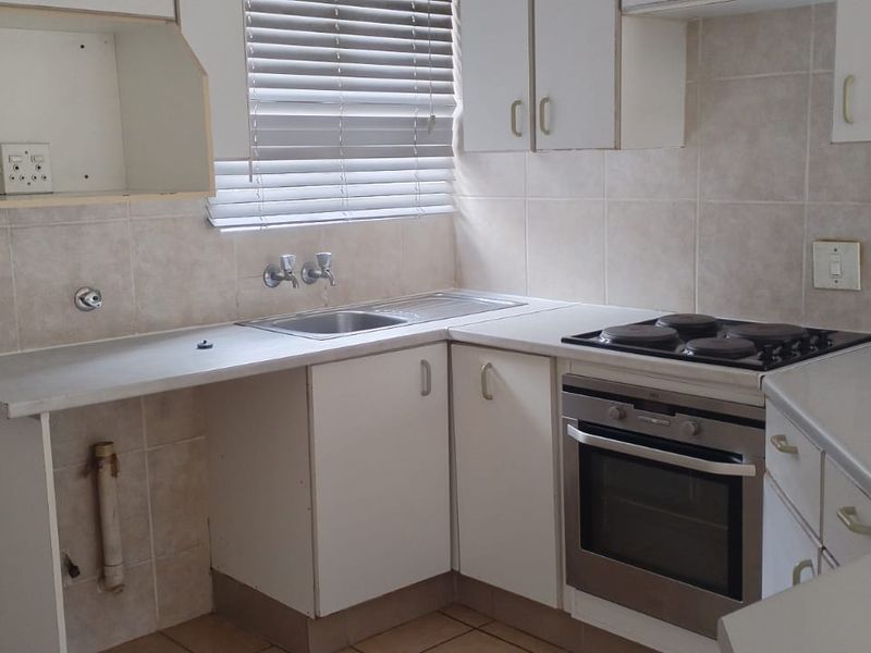 A functional kitchen featuring built-in cabinetry, a stainless steel sink, and an integrated electric oven and hob with tiled backsplash.