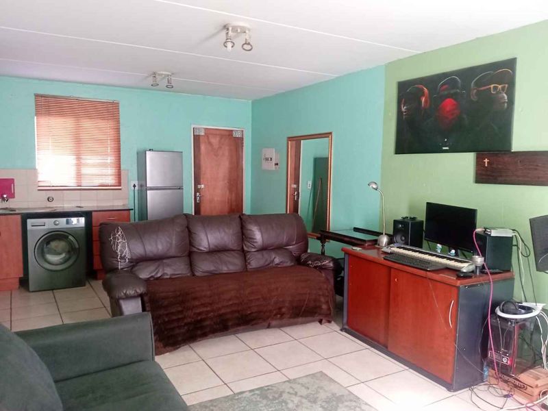 Open-plan living area featuring tiled flooring and a compact kitchen corner with built-in cabinetry and laundry plumbing.