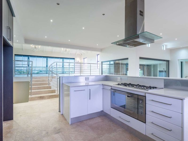 Spacious open-plan kitchen featuring modern cabinetry, stone countertops, and integrated appliances, overlooking a split-level living area with a feature staircase.