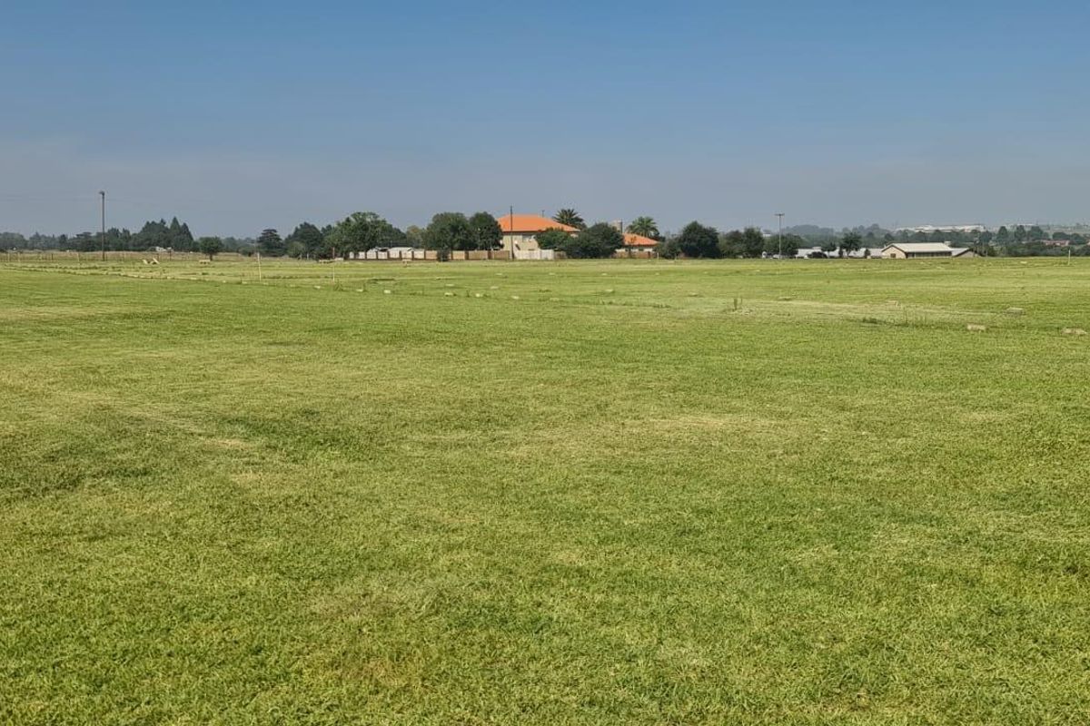 A wide-angle view of a flat, expansive agricultural land parcel featuring well-maintained grass coverage and distant rural surroundings.