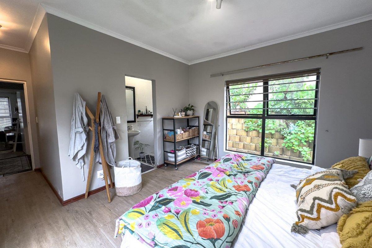 A bedroom featuring laminate flooring, large aluminium-framed windows with security bars, and an adjoining en-suite bathroom.