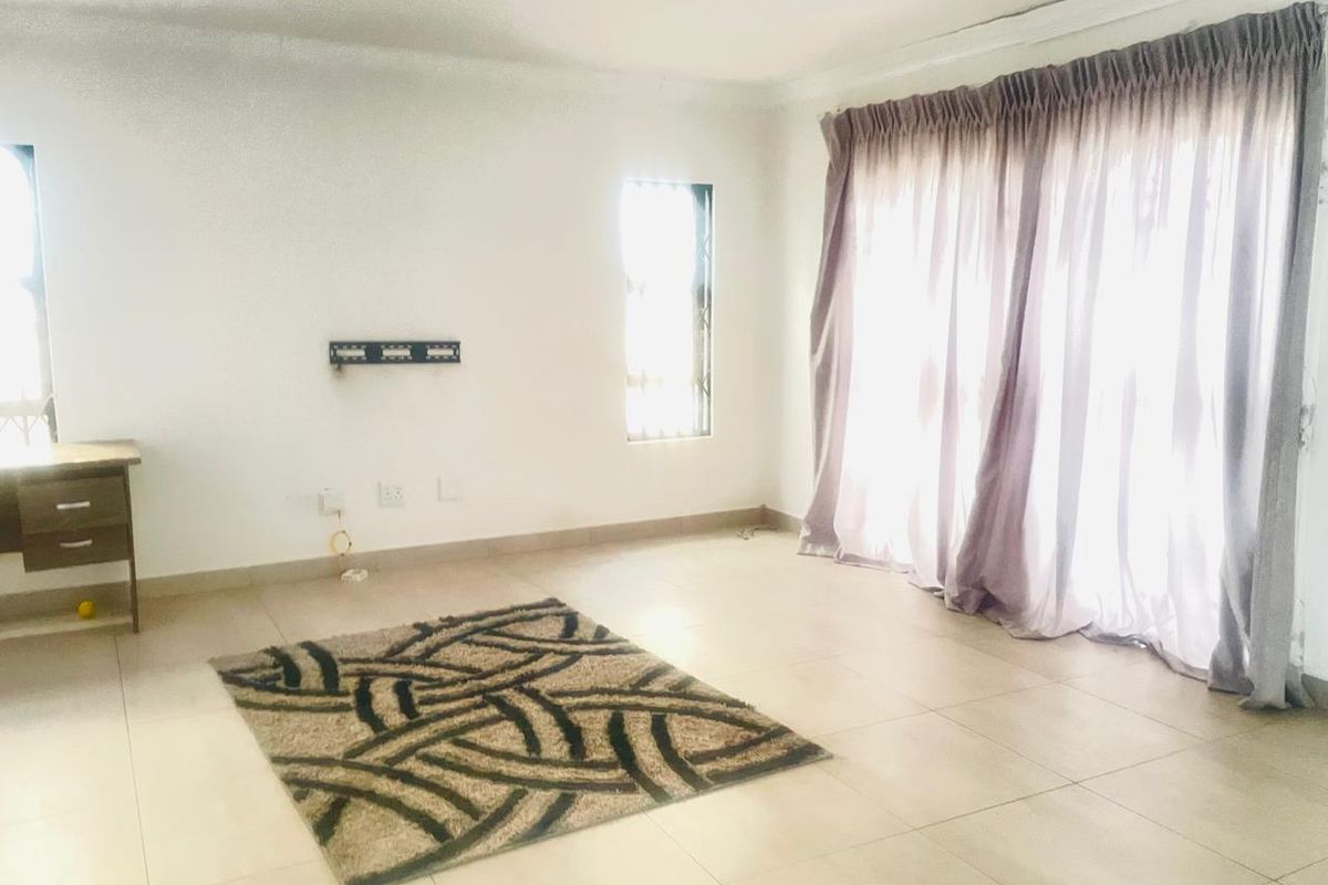 A bright, open-plan living area featuring neutral floor tiles, large sliding doors with curtains, and a wall-mounted television bracket.