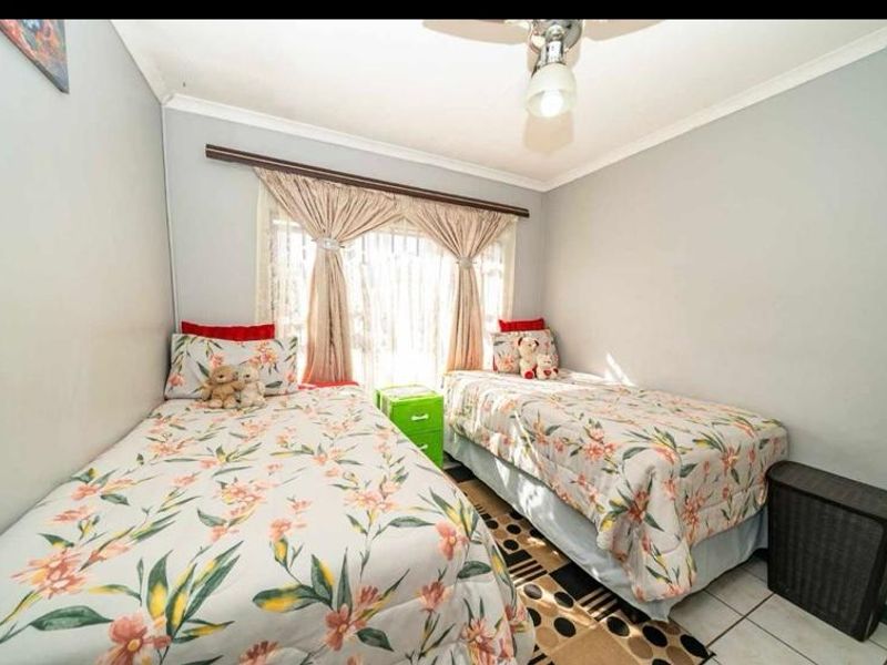 A compact bedroom featuring tiled flooring, a ceiling fan, and a large window with curtain rod installation.