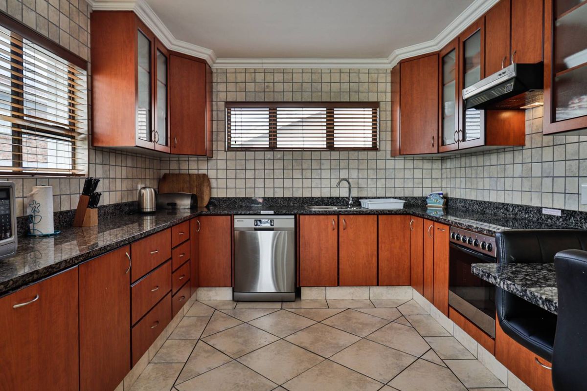 A functional U-shaped kitchen featuring dark granite countertops, wood-veneer cabinetry, tiled splashbacks, and integrated stainless steel appliances.