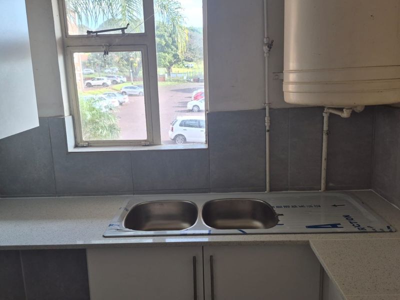 A functional kitchen area featuring a double bowl stainless steel sink, quartz countertops, and built-in cabinetry with a tiled backsplash.