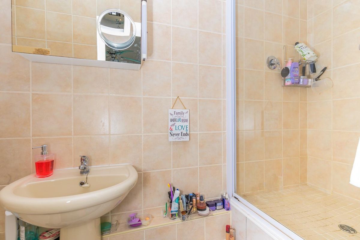 A functional bathroom featuring a pedestal basin, wall-mounted mirror cabinet, and a tiled shower enclosure with a glass door.
