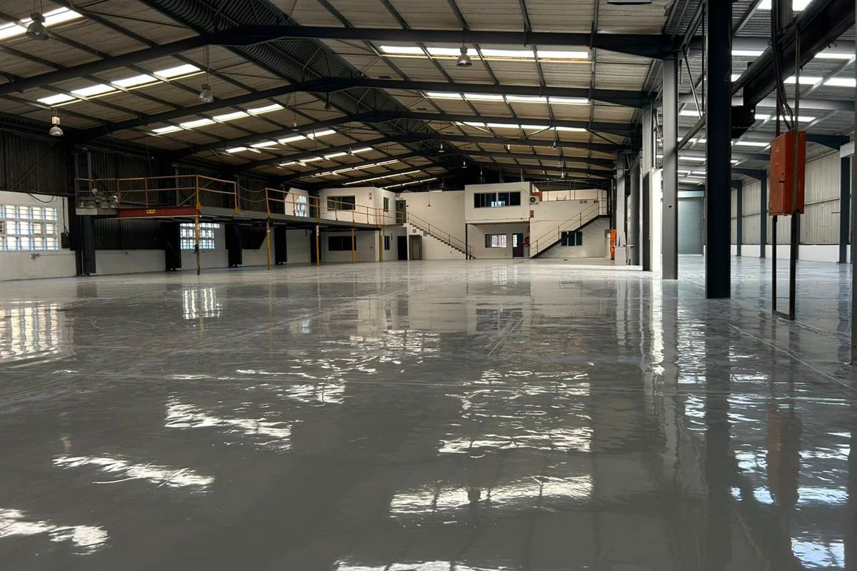 Spacious industrial warehouse featuring a high-gloss epoxy floor, steel portal frame construction, mezzanine level, and ample natural light through integrated skylights.