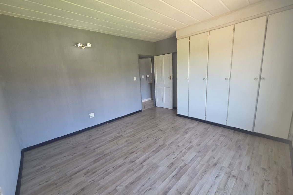 A spacious, empty bedroom featuring light-toned laminate flooring, built-in cupboards, and a neutral grey wall finish, ready for personalization.
